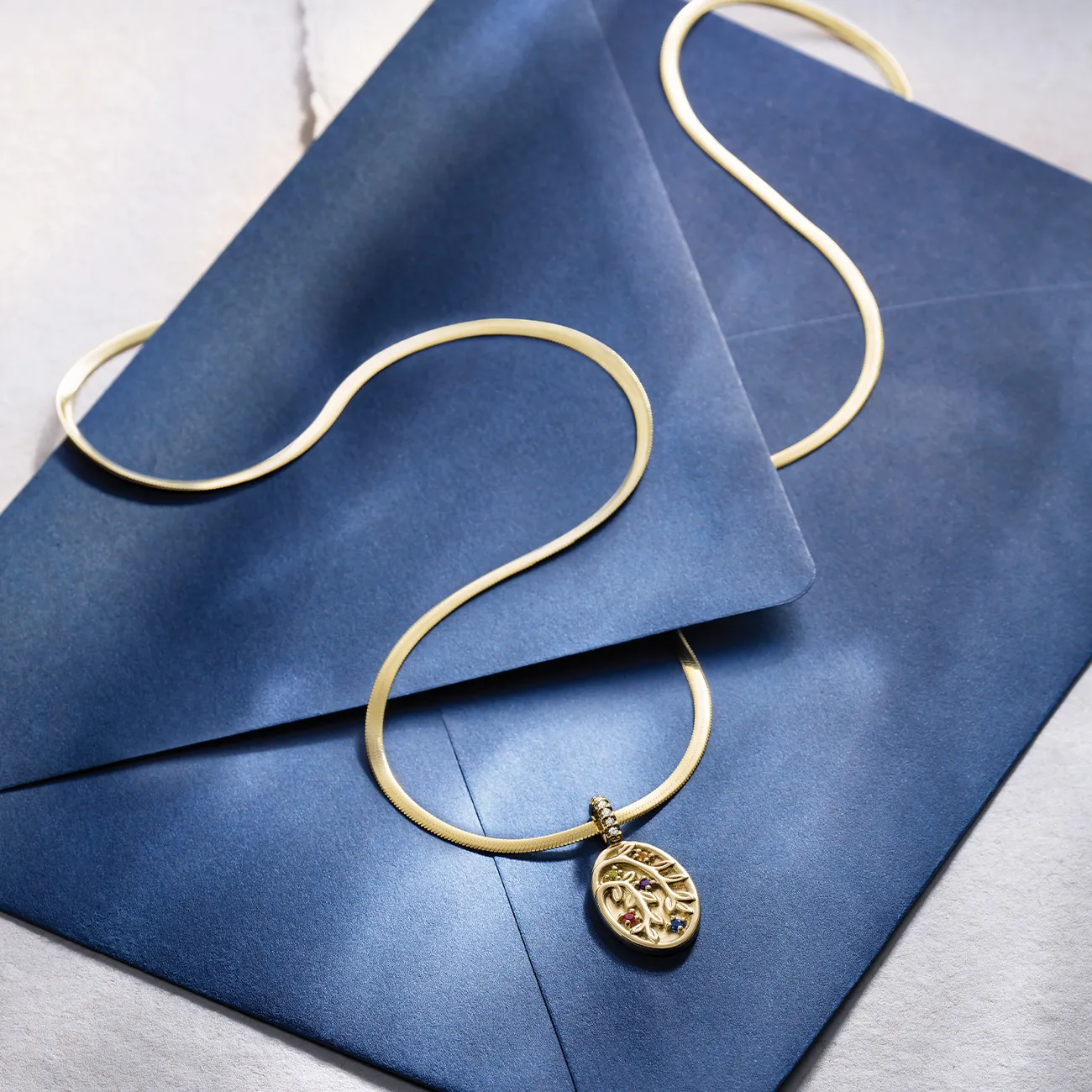 Gold necklace with pendant on blue envelopes.
