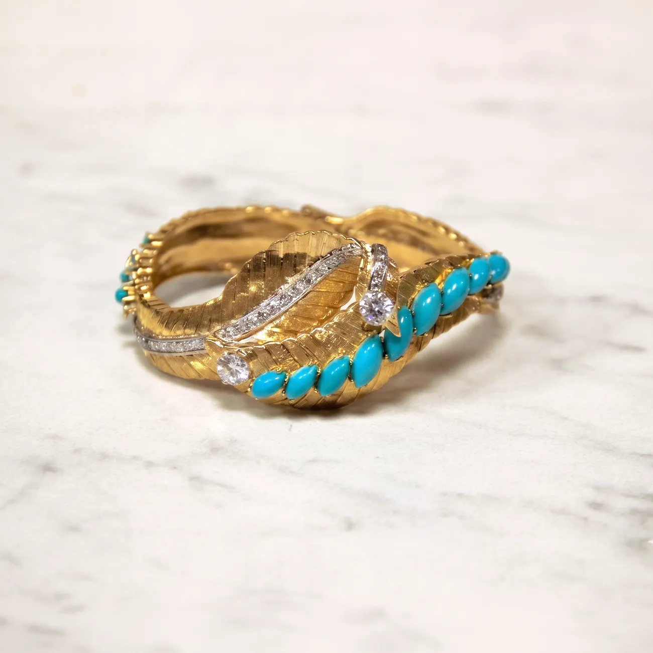 A gold ring with turquoise stones and diamonds on a marble surface.