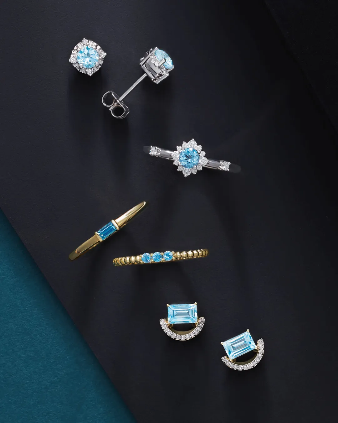 A collection of blue gemstone jewelry, including rings, earrings, and a bracelet, displayed on a dark background.