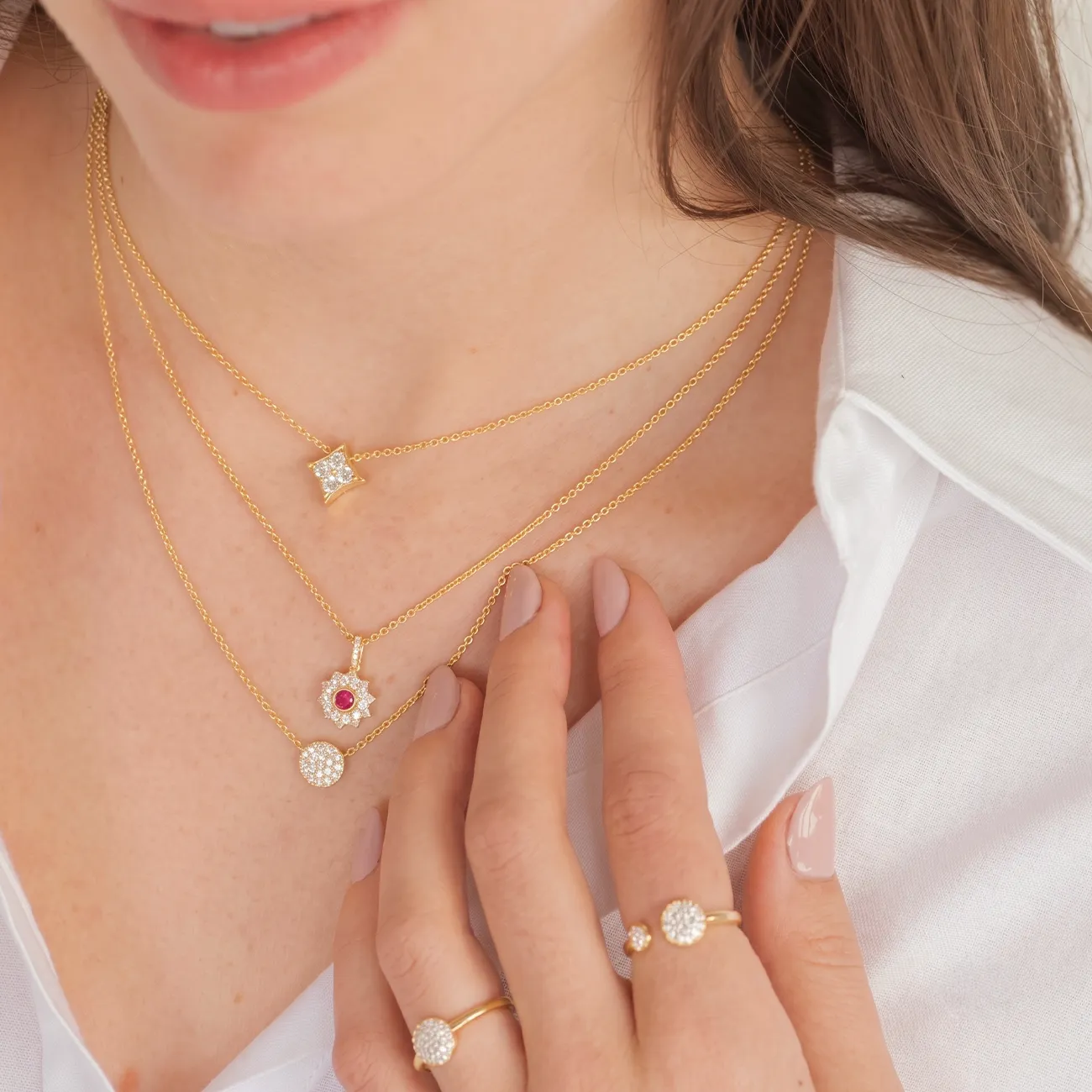 Layered gold necklaces with diamond and ruby pendants, worn with matching rings.