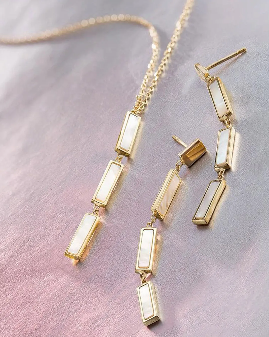 Gold necklace and earrings with rectangular pearl inlays on a soft pink surface.
