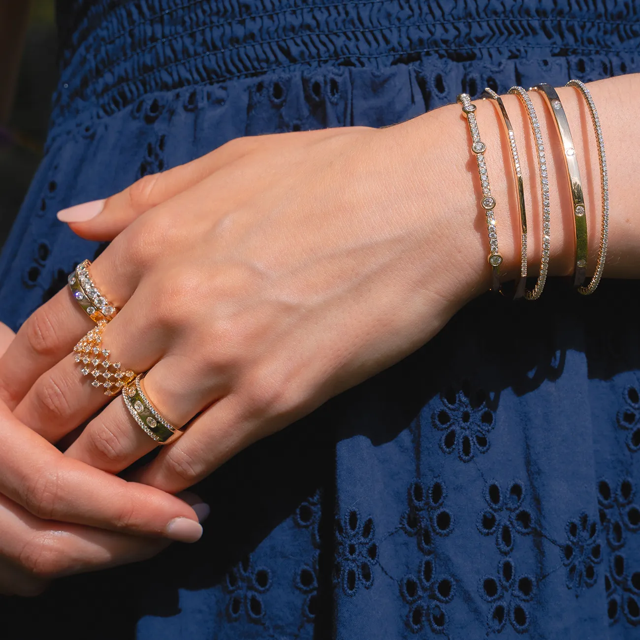 Hands adorned with gold and diamond rings and bracelets against a blue dress.