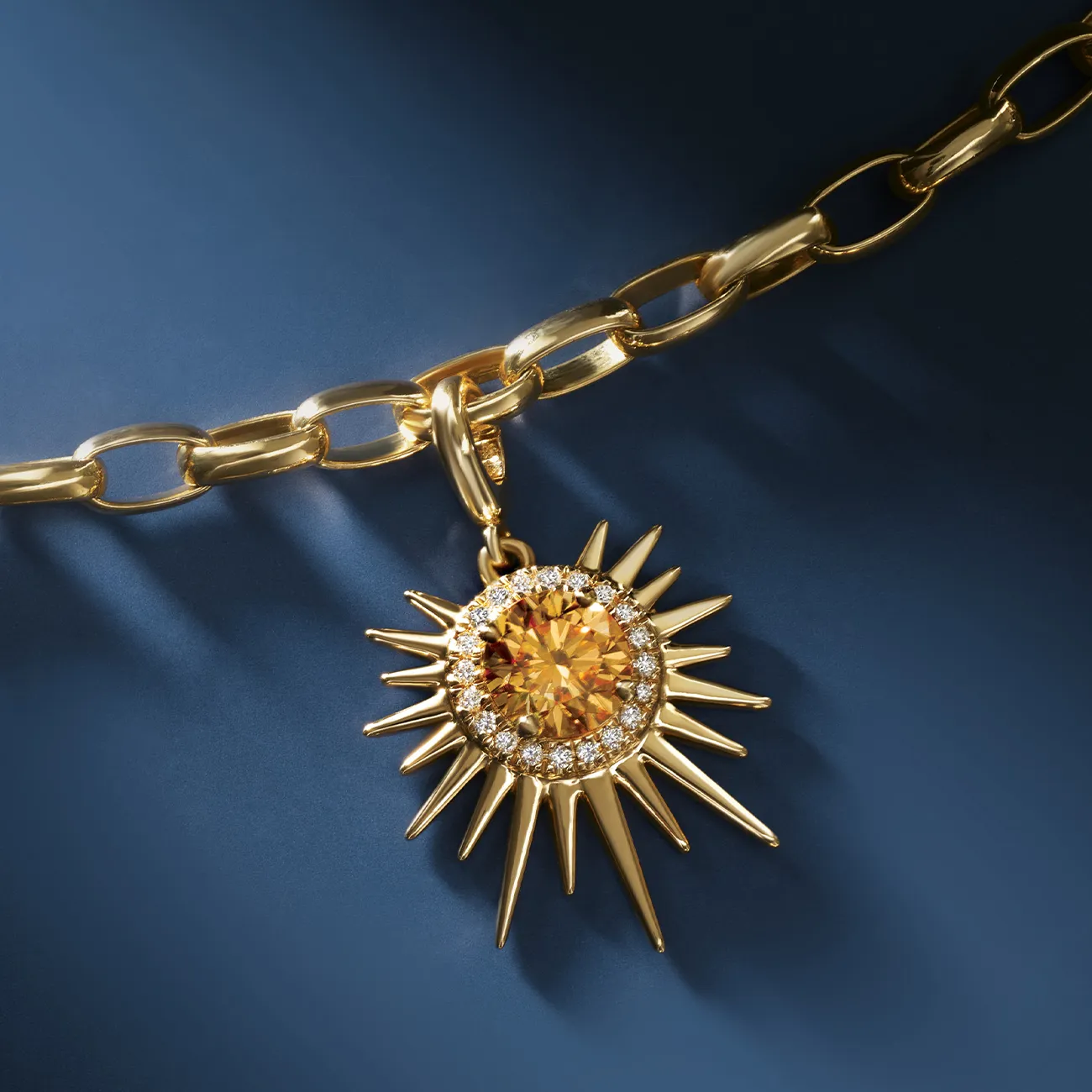 A gold chain with a sunburst pendant featuring a central amber stone and surrounding diamonds on a blue background.