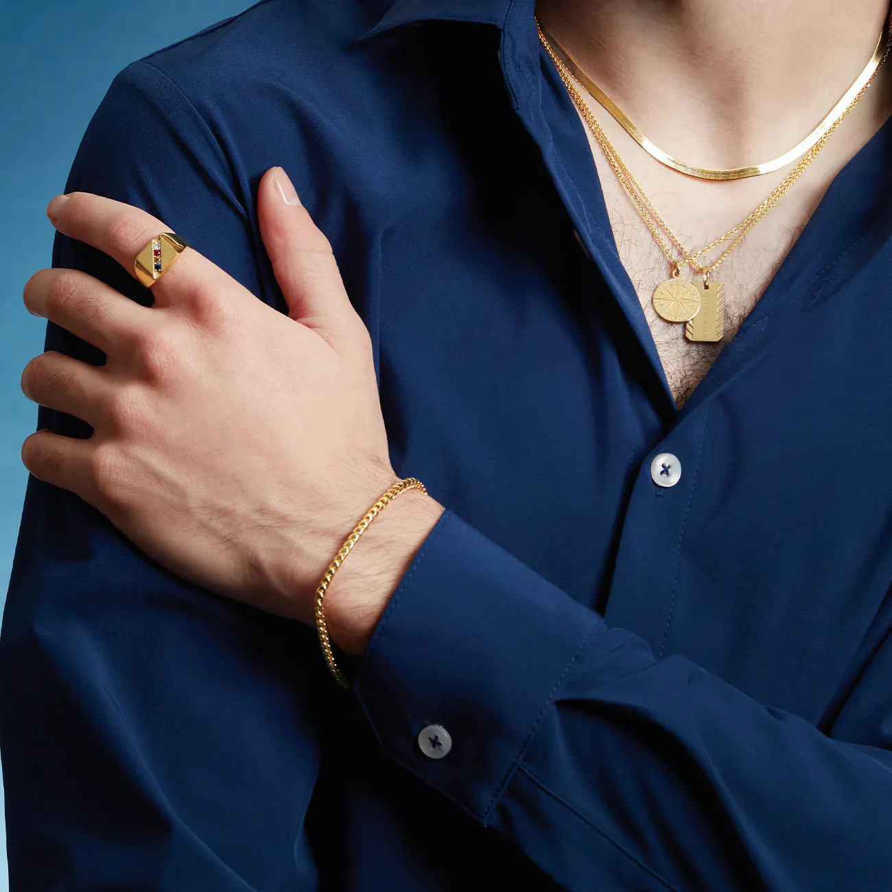 Man in blue shirt wearing gold jewelry: necklace, bracelet, and ring.