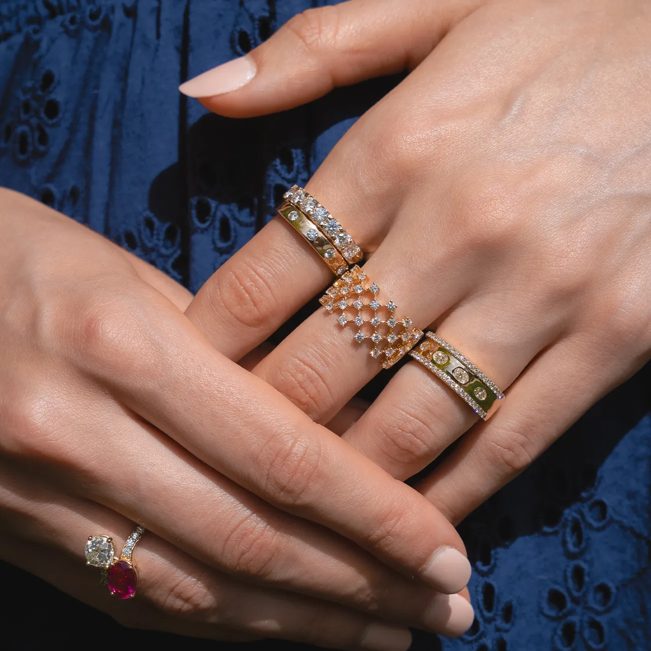 Hands displaying multiple gold rings with diamonds and gemstones.