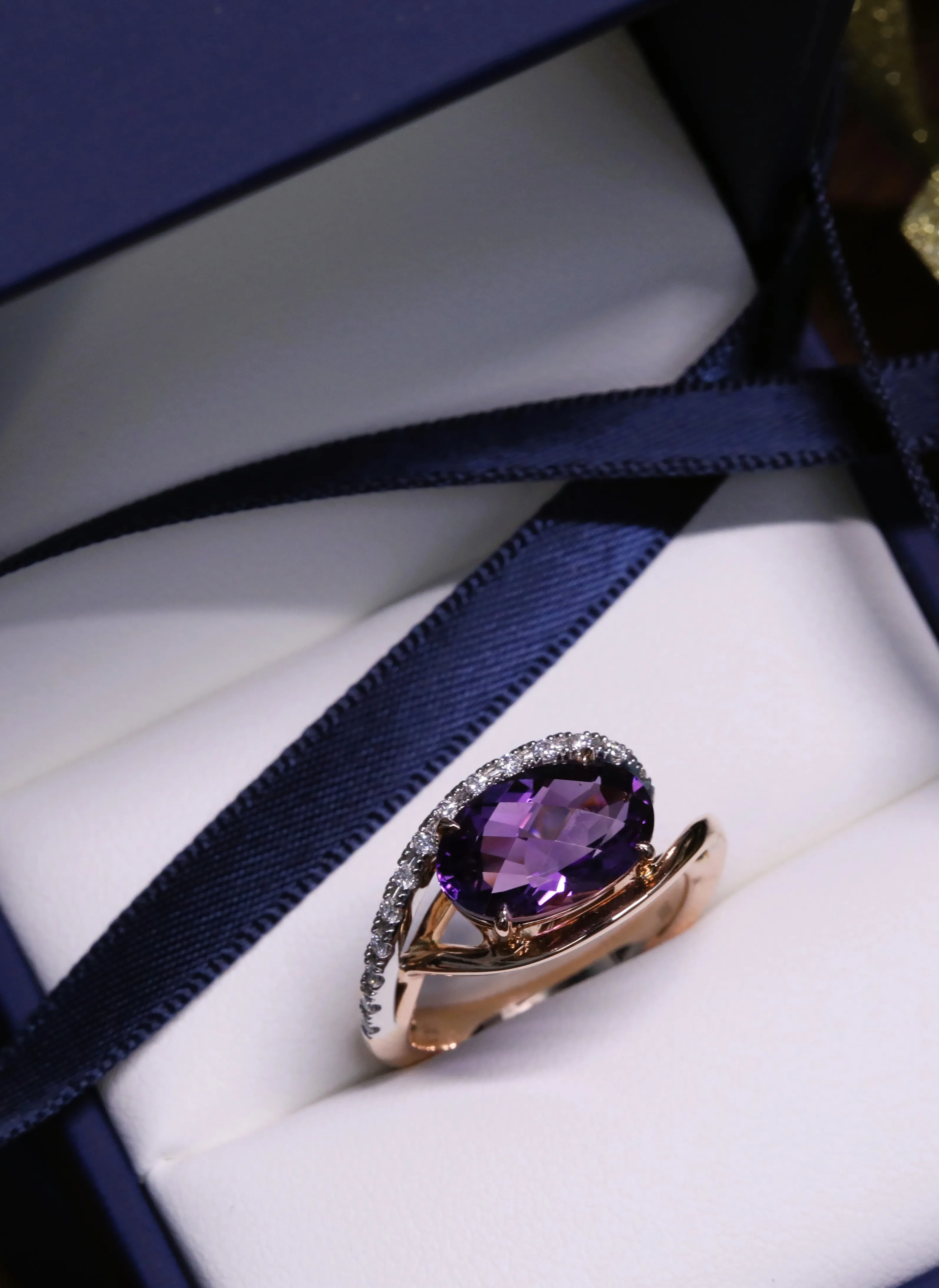 Elegant rose gold ring featuring a purple gemstone and diamond accents, displayed in a jewelry box.