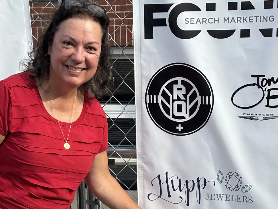 A woman named Angela Peterson smiling next to a banner at a community event in Fishers, IN.