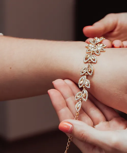 A hand is fastening a sparkling gold bracelet adorned with diamonds on another wrist.