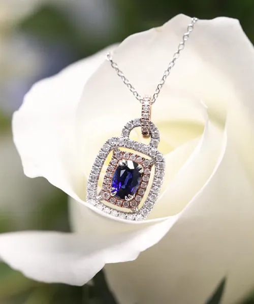 Elegant sapphire pendant necklace set in diamonds, displayed on a white rose. Visit Hupp Jewelers in Fishers for more.