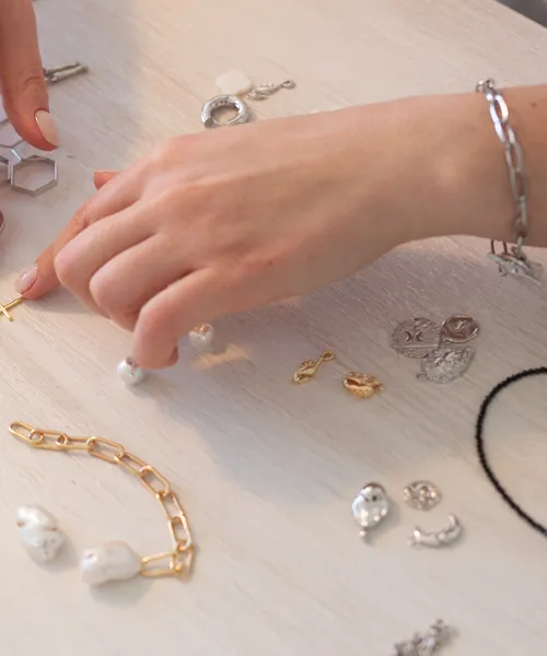 A hand selecting jewelry pieces on a table, showcasing various earrings, bracelets, and charms.