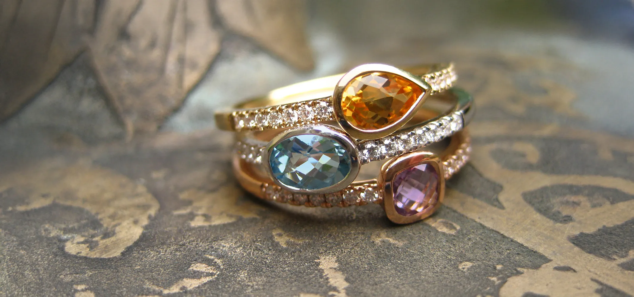 Colorful gemstone rings stacked together on a textured surface. 