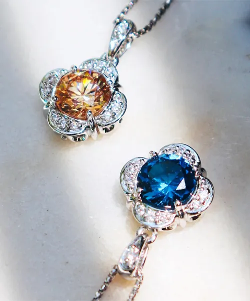 Elegant silver pendants featuring a golden and a blue gemstone, adorned with sparkling diamonds. 