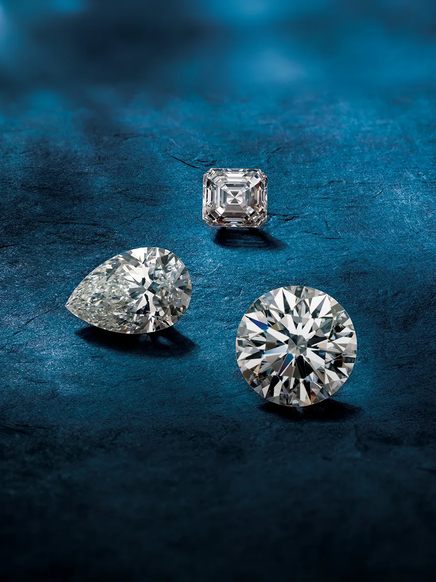 Three diamonds in different cuts (round, pear, square) on a textured blue surface.