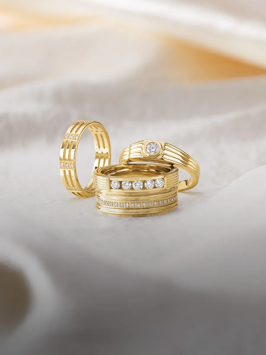 Four gold rings with diamond accents displayed on a soft, light-colored fabric.