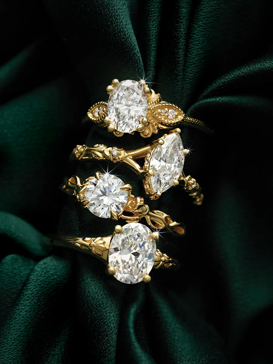 Four gold rings with large oval diamonds on dark green fabric background.