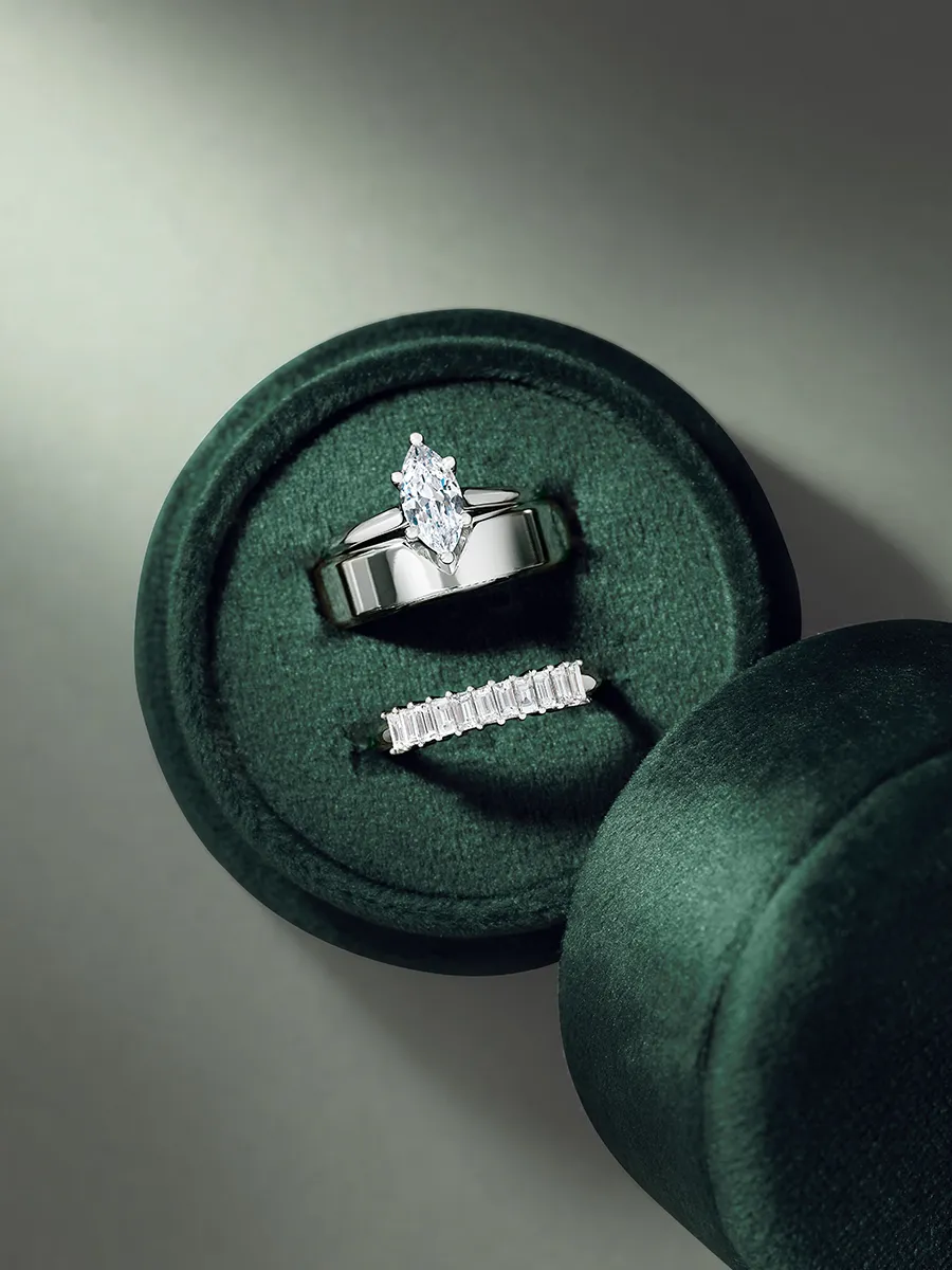 Two diamond rings in a green velvet box, one with a marquise cut stone and the other with baguette diamonds.