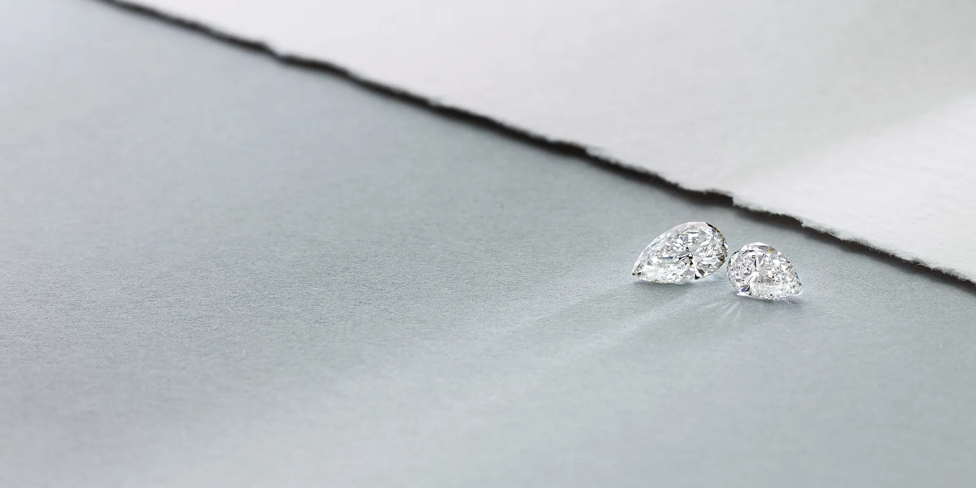 Two pear-shaped diamonds on a textured gray surface.