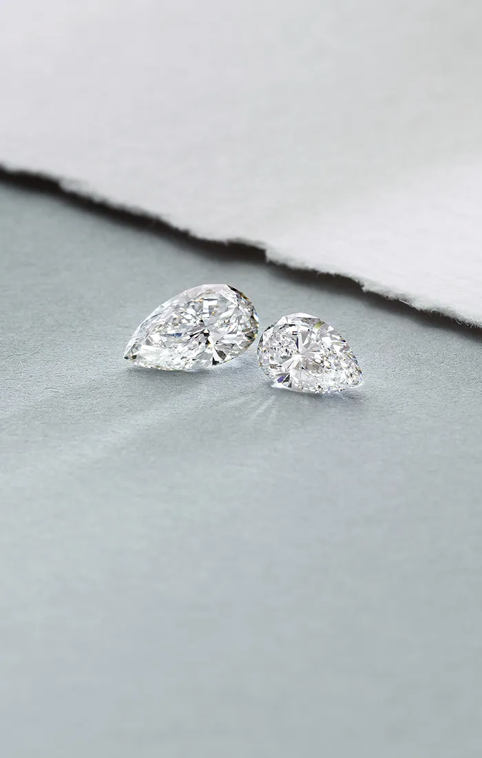 Two pear-shaped diamonds on a textured gray surface.