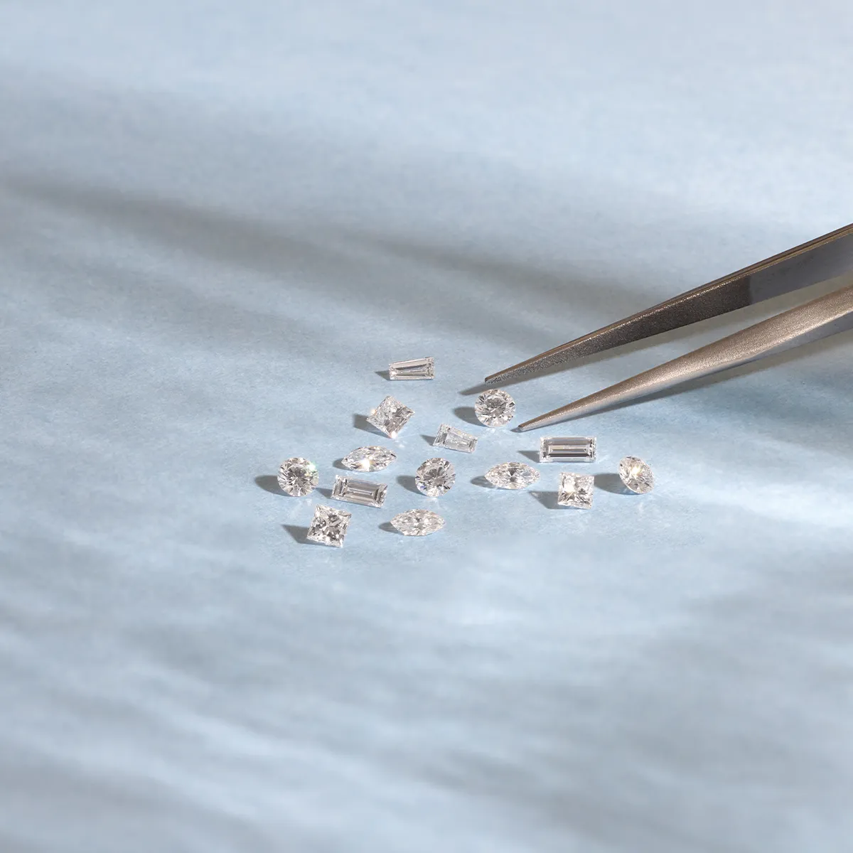 A collection of small, sparkling diamonds on a light blue surface with tweezers.