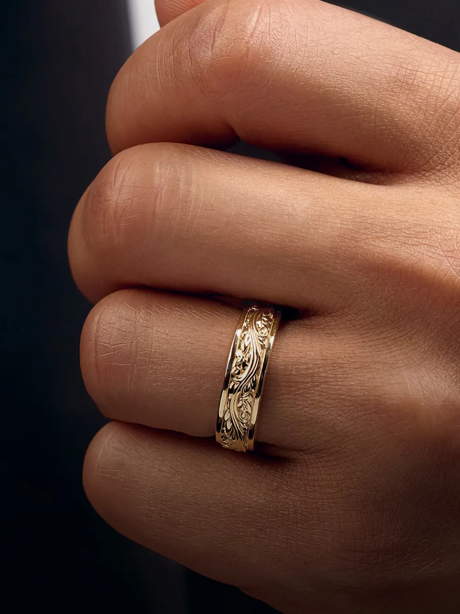 A hand wearing a gold wedding band with intricate engravings.