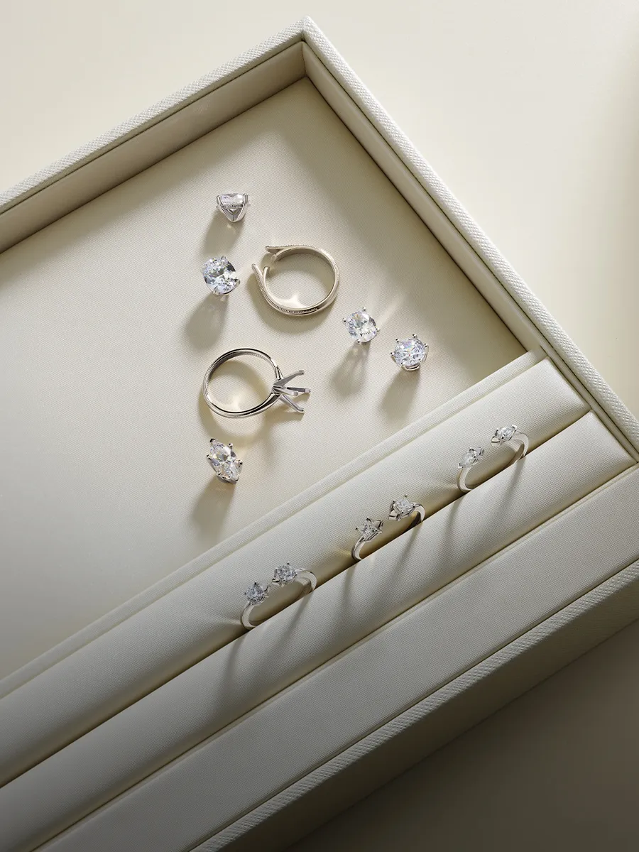 Elegant diamond rings and loose stones displayed in a cream jewelry box.