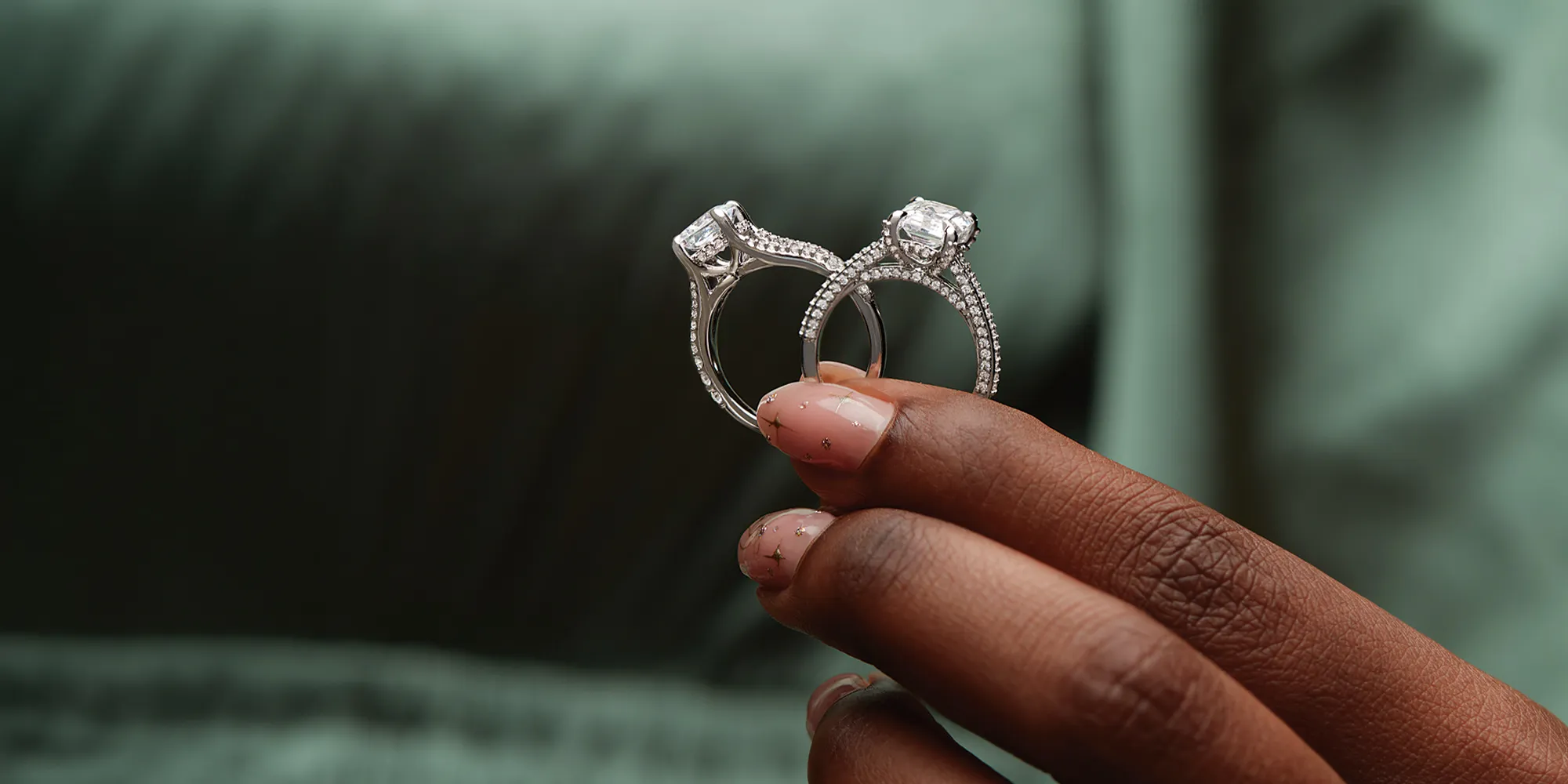 A hand holding two diamond engagement rings with intricate designs.