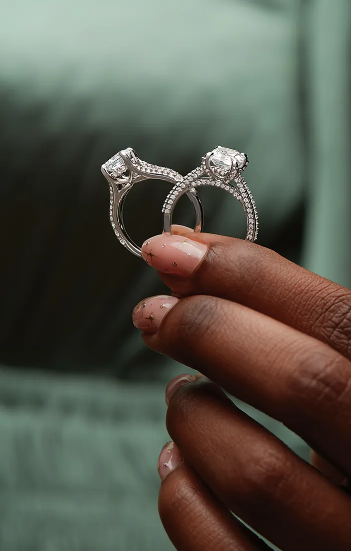 A hand holding two diamond engagement rings with intricate designs.