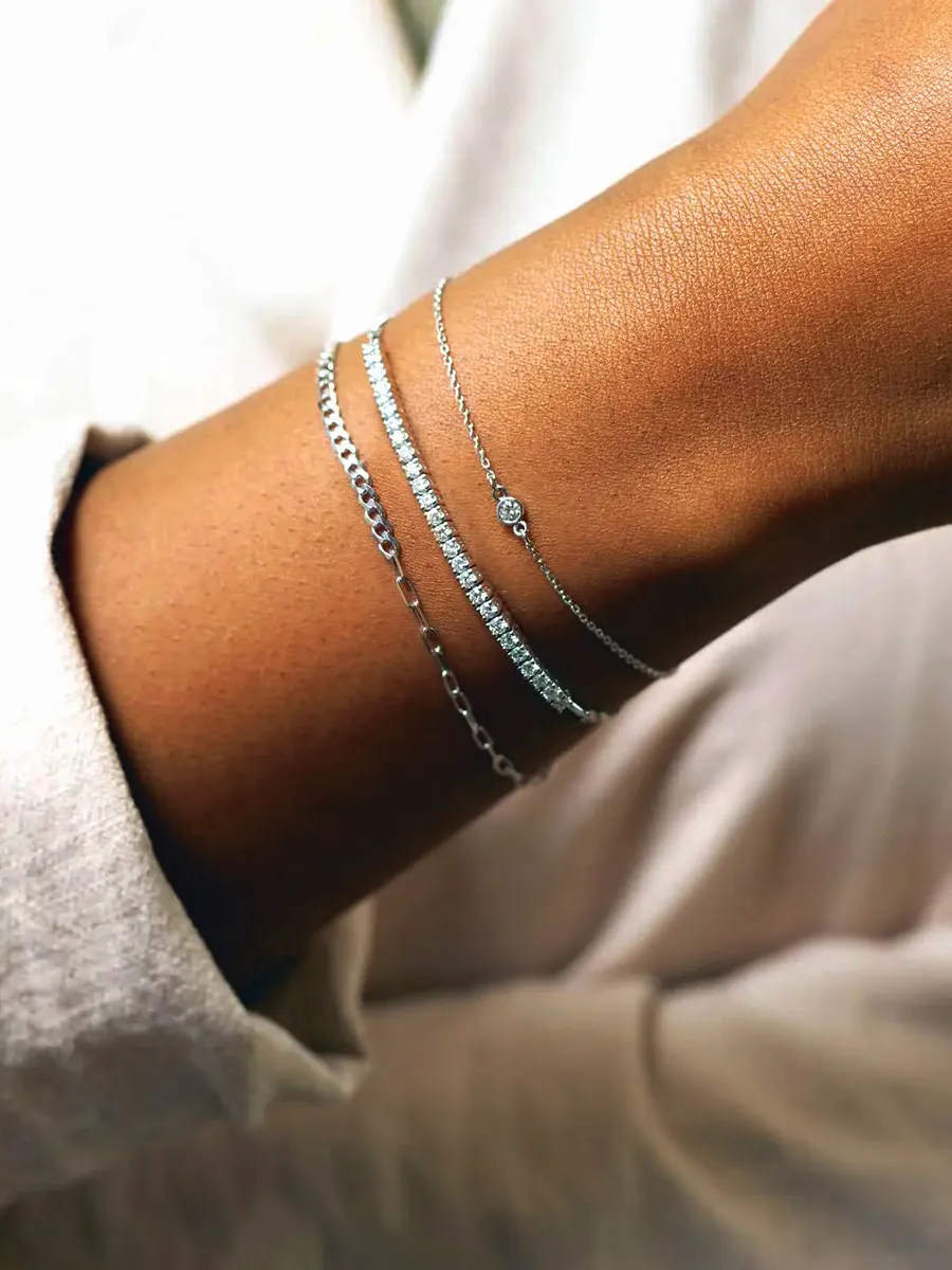 A wrist adorned with three delicate silver bracelets, including a chain and a diamond-studded design.