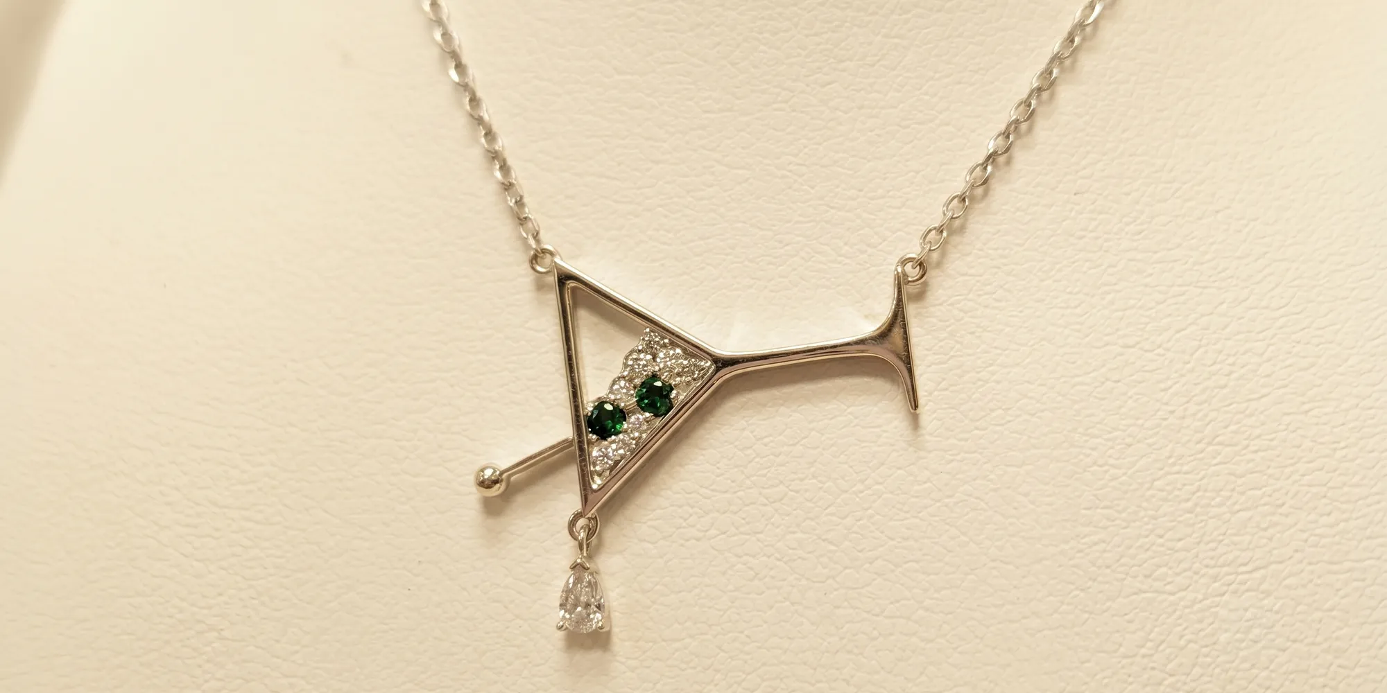 Silver necklace with martini glass pendant, green gems, and a dangling teardrop gem.