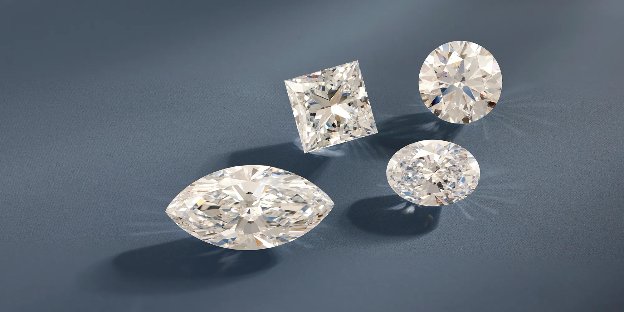 Four sparkling diamonds in different cuts on a blue surface.