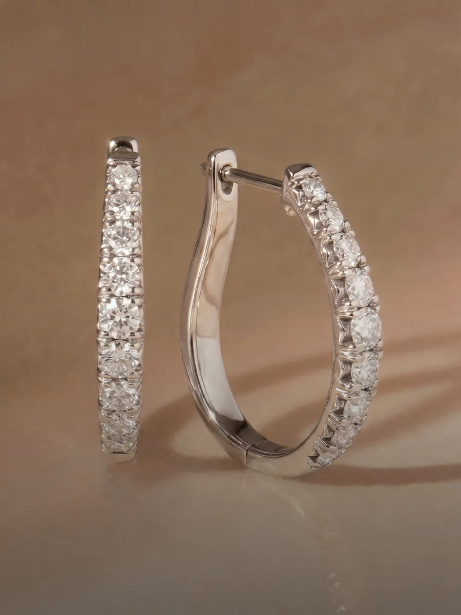 Elegant diamond hoop earrings on a soft beige background.