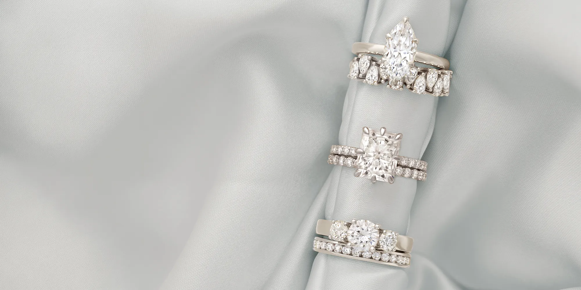 Three diamond engagement rings with different settings on a light fabric background.