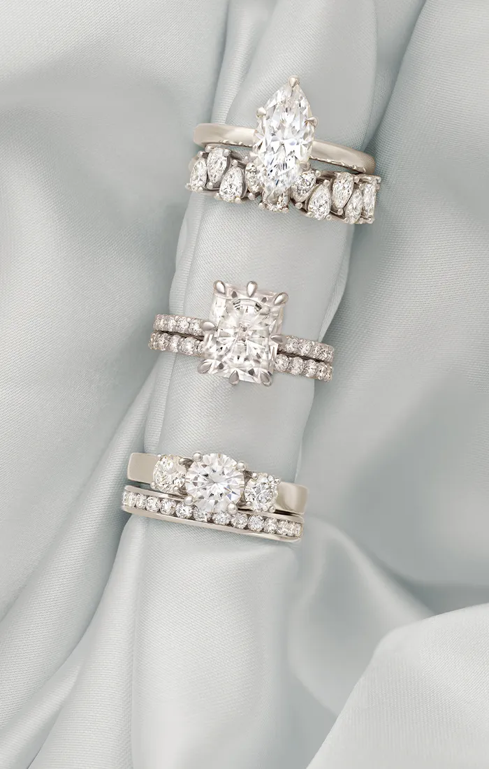 Three diamond engagement rings with different settings on a light fabric background.