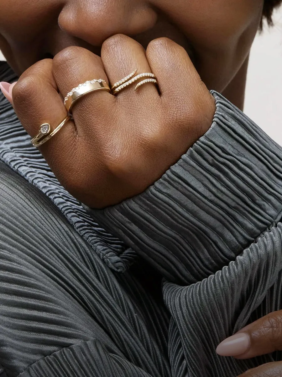A hand wearing multiple gold rings with a textured gray sleeve.