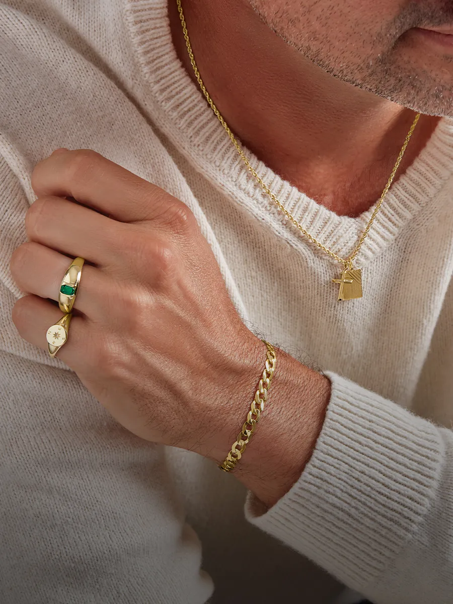Man wearing gold necklace, bracelet, and rings with a white sweater.