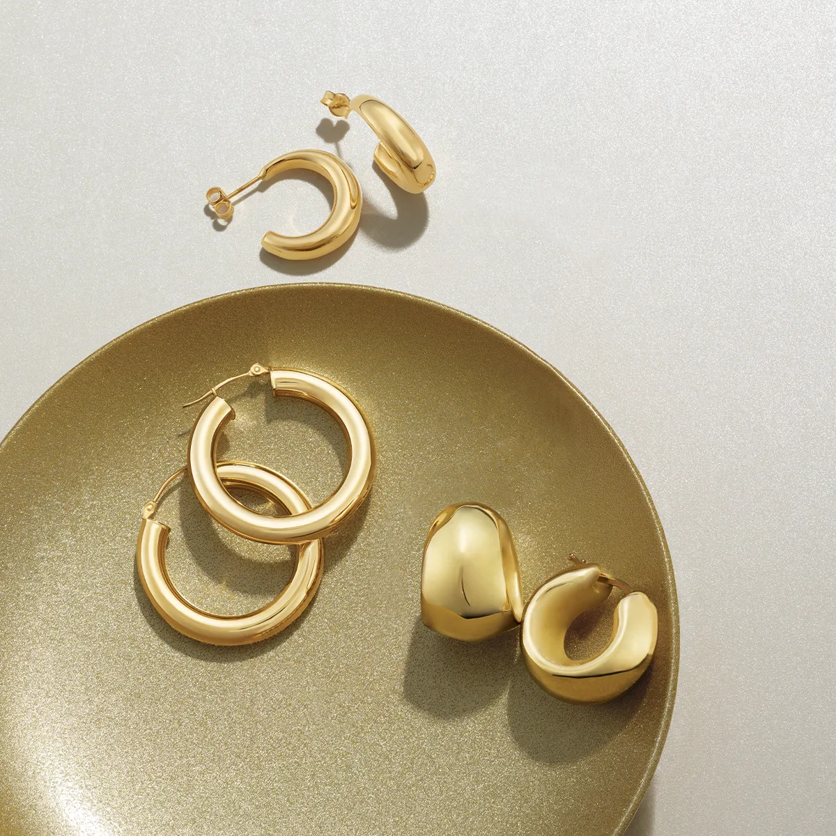 Golden hoop earrings displayed on a shimmering gold plate.