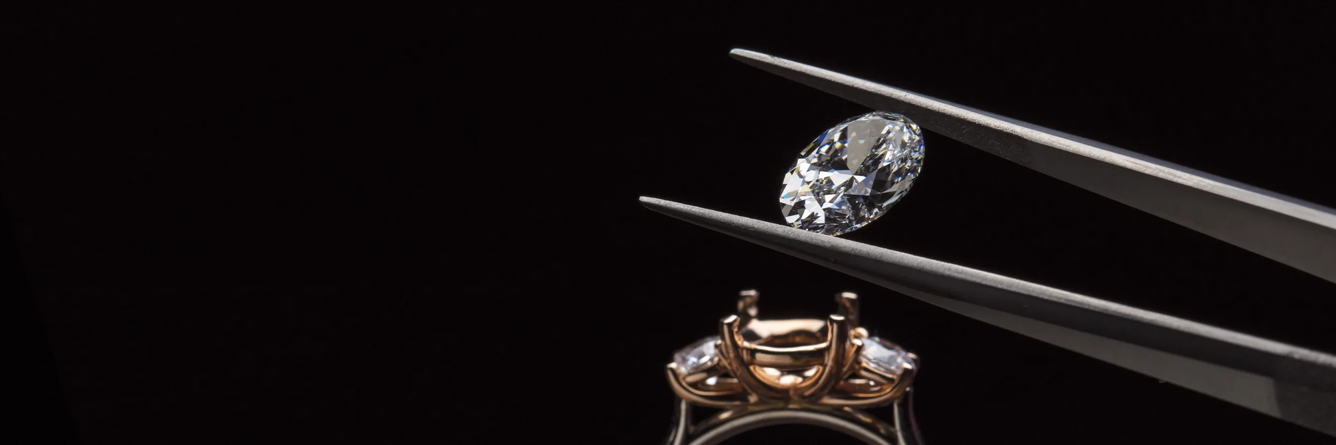 A diamond held by tweezers above a ring setting, ready for placement.