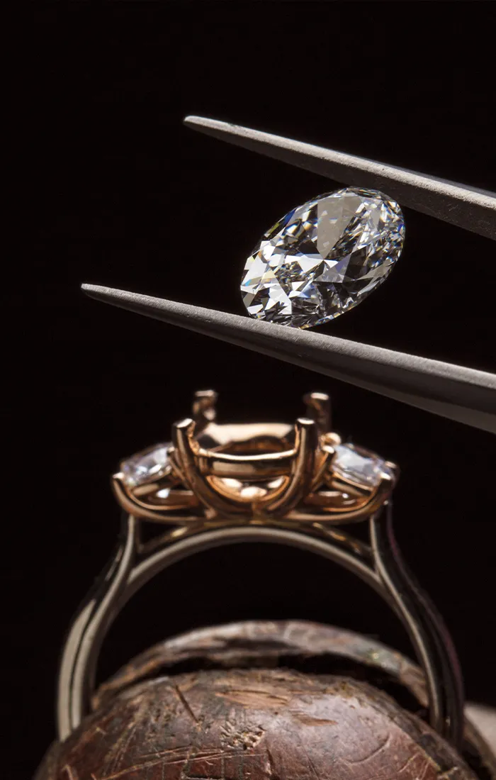 A diamond held by tweezers above a ring setting, ready for placement.