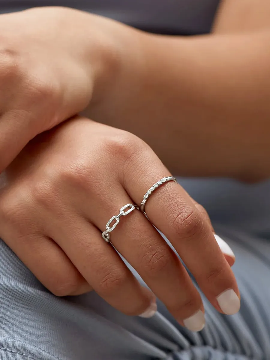 Two hands with manicured nails wearing two silver rings, one with a chain design and the other with small stones.