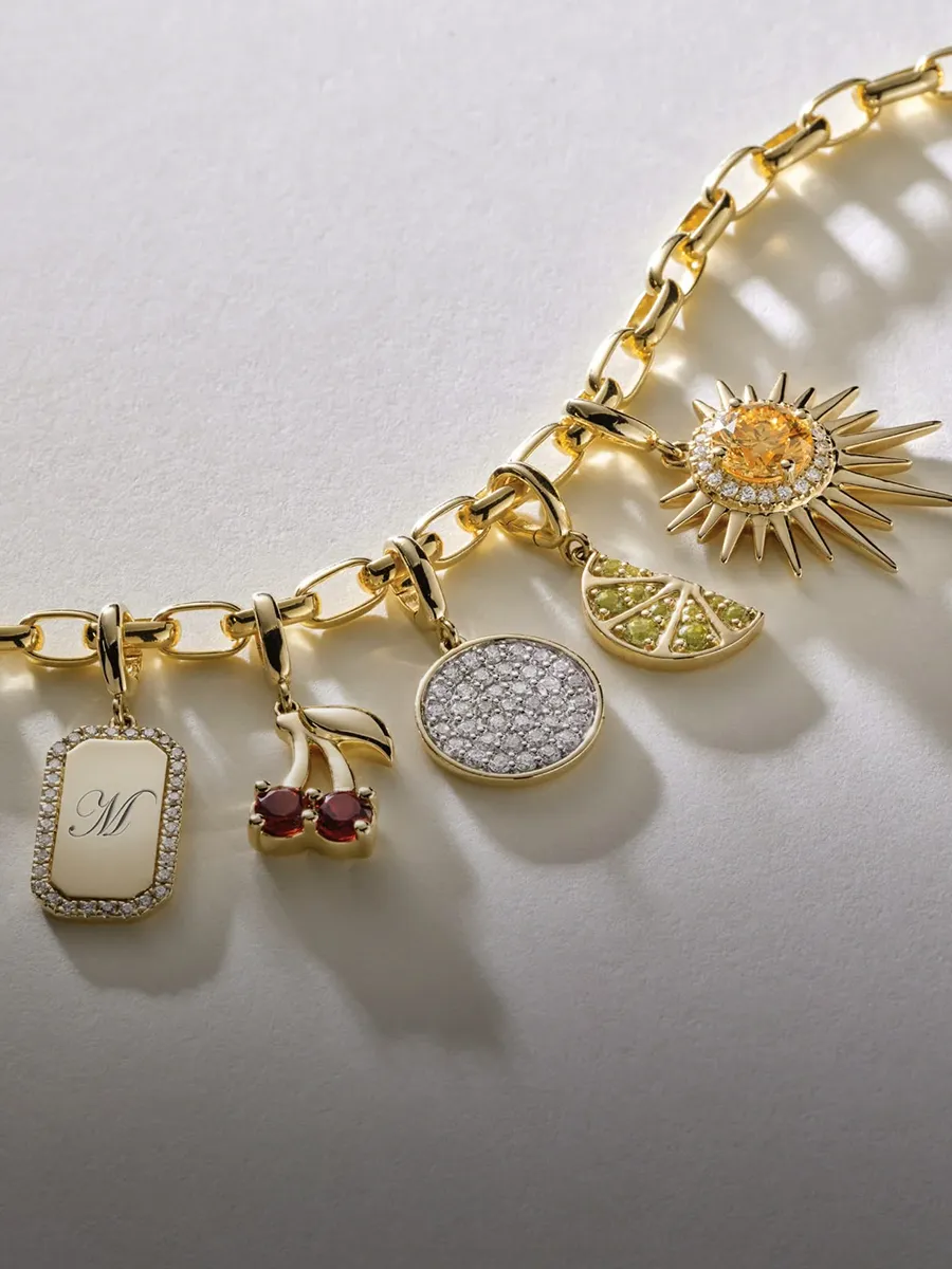 A gold charm bracelet with various pendants including a sun, cherries, and a monogrammed tag.
