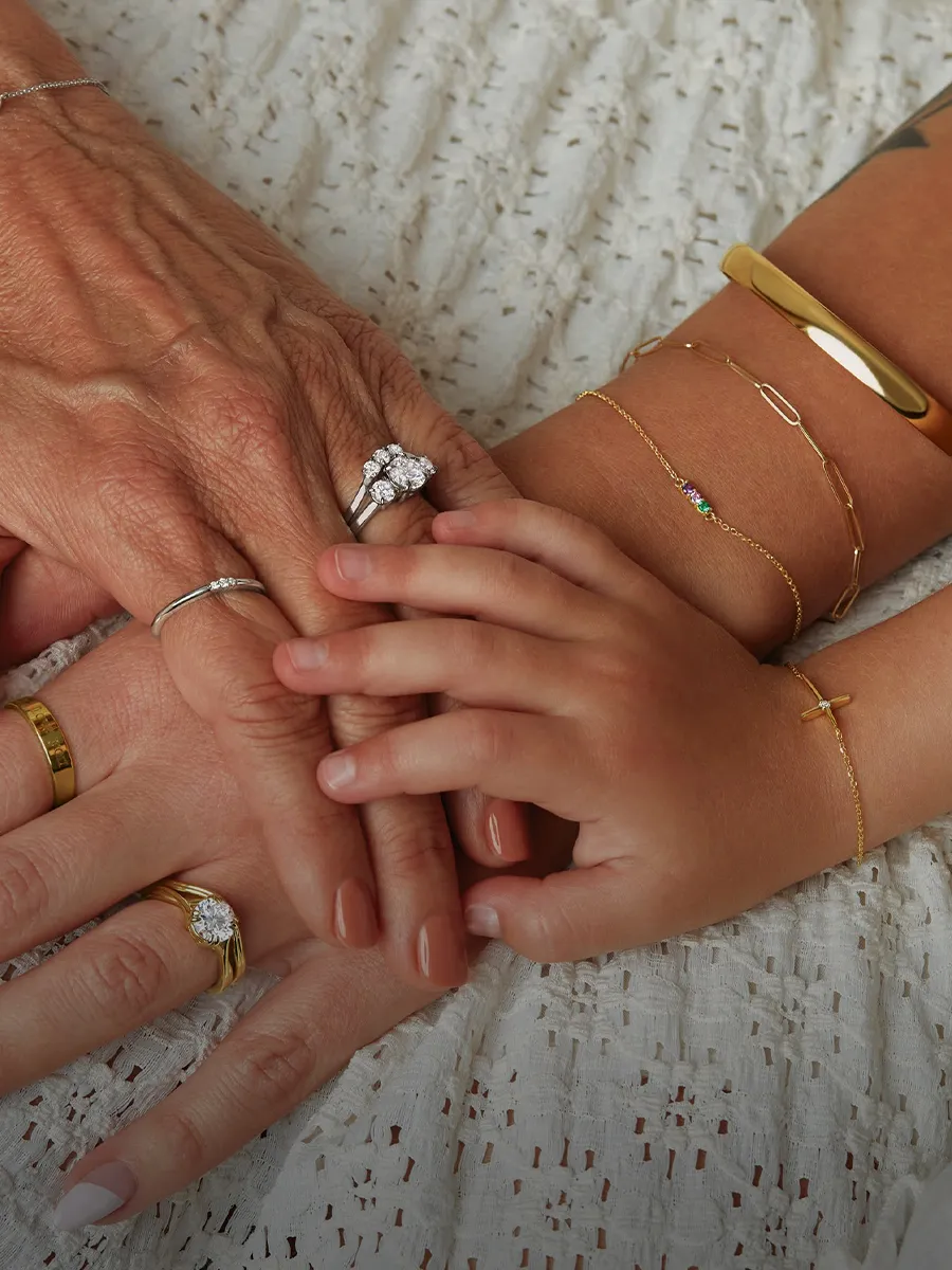 Hands of different ages with rings and bracelets on a lace fabric background.