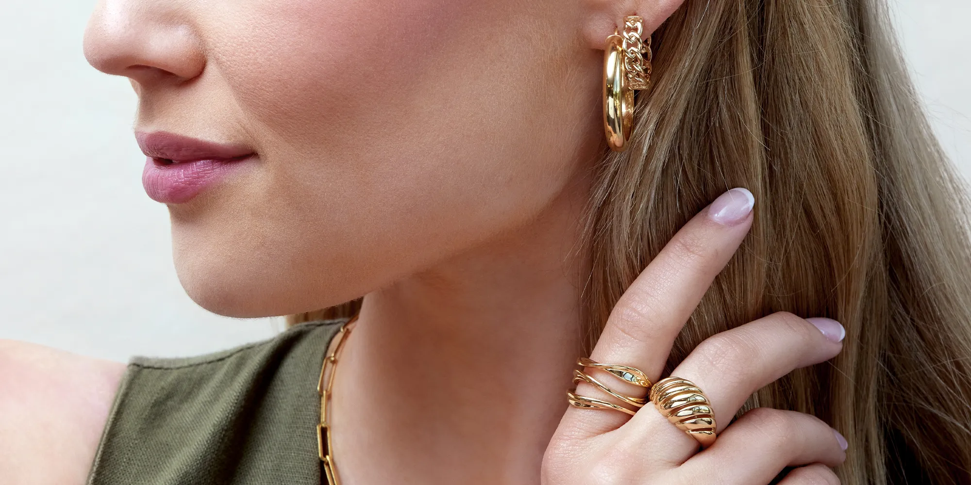 A woman wearing gold hoop earrings and multiple gold rings, with her hand near her face.