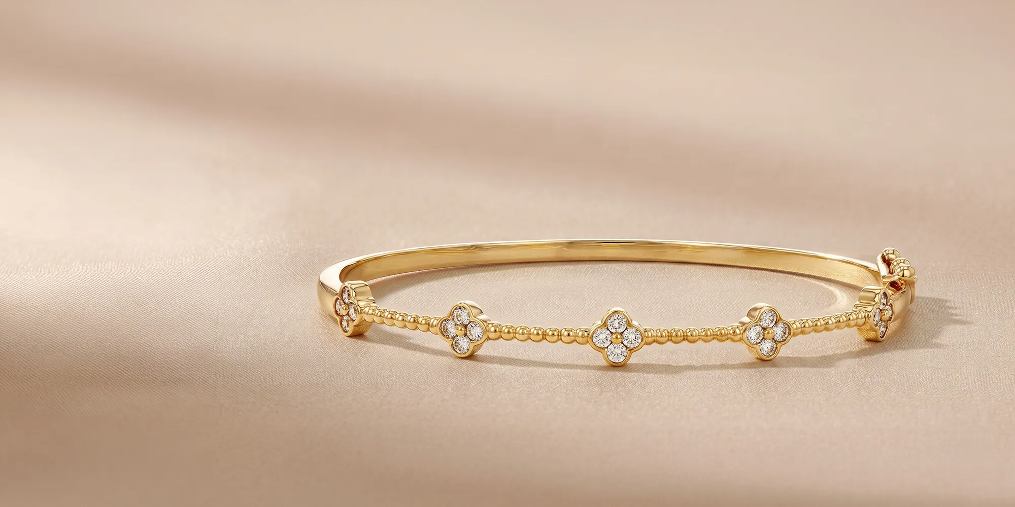 Elegant gold bracelet with diamond-studded floral motifs on a beige background.