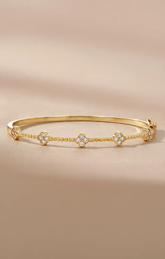 Elegant gold bracelet with diamond-studded floral motifs on a beige background.