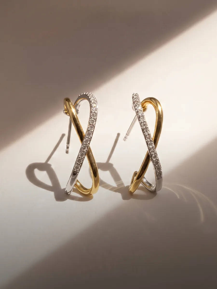 Gold and silver intertwined earrings with diamond accents on a light background.