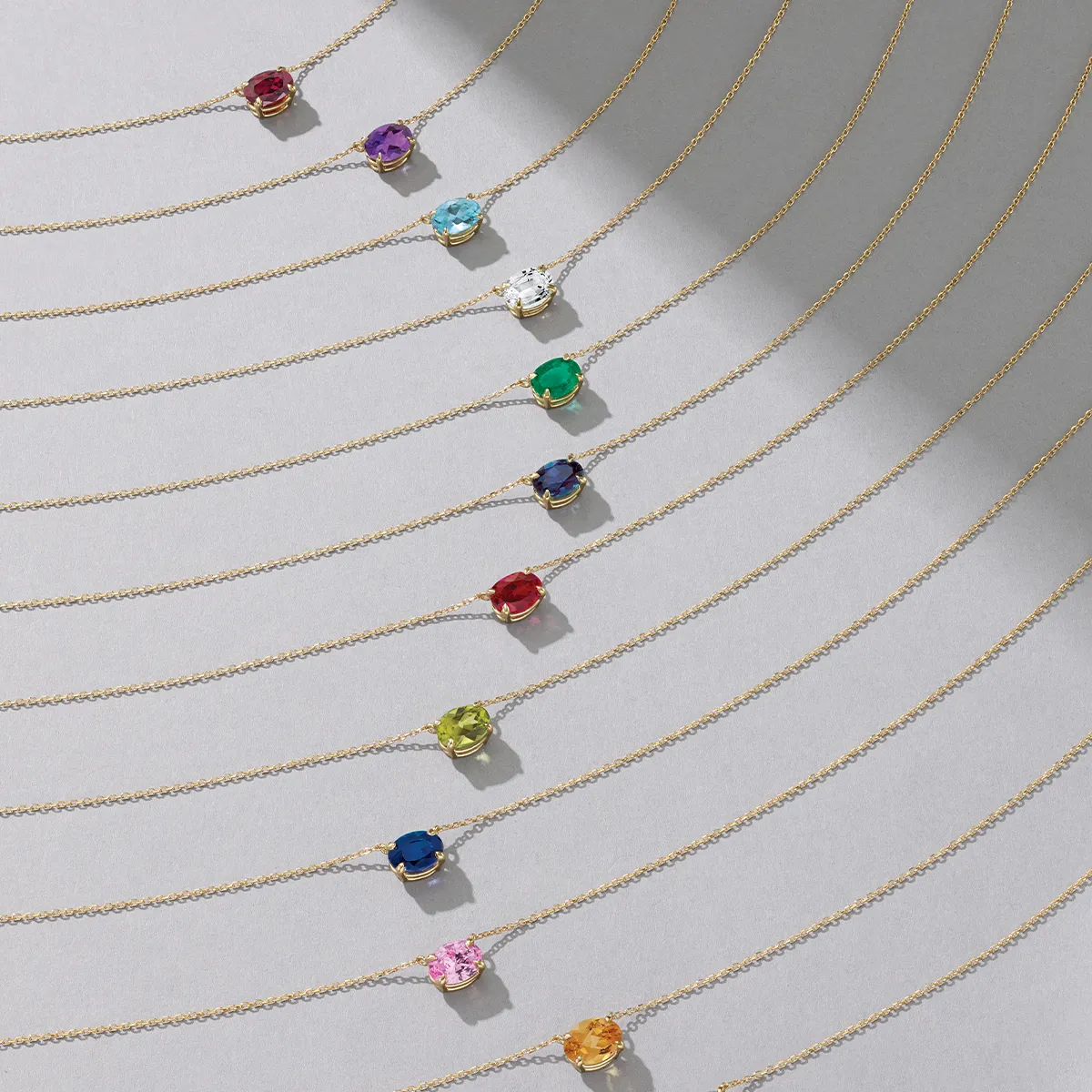 A collection of gold necklaces with colorful gemstone pendants arranged in a curved pattern on a gray background.