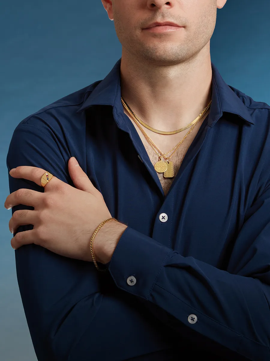 A man in a blue shirt wearing multiple gold necklaces, a bracelet, and a ring.
