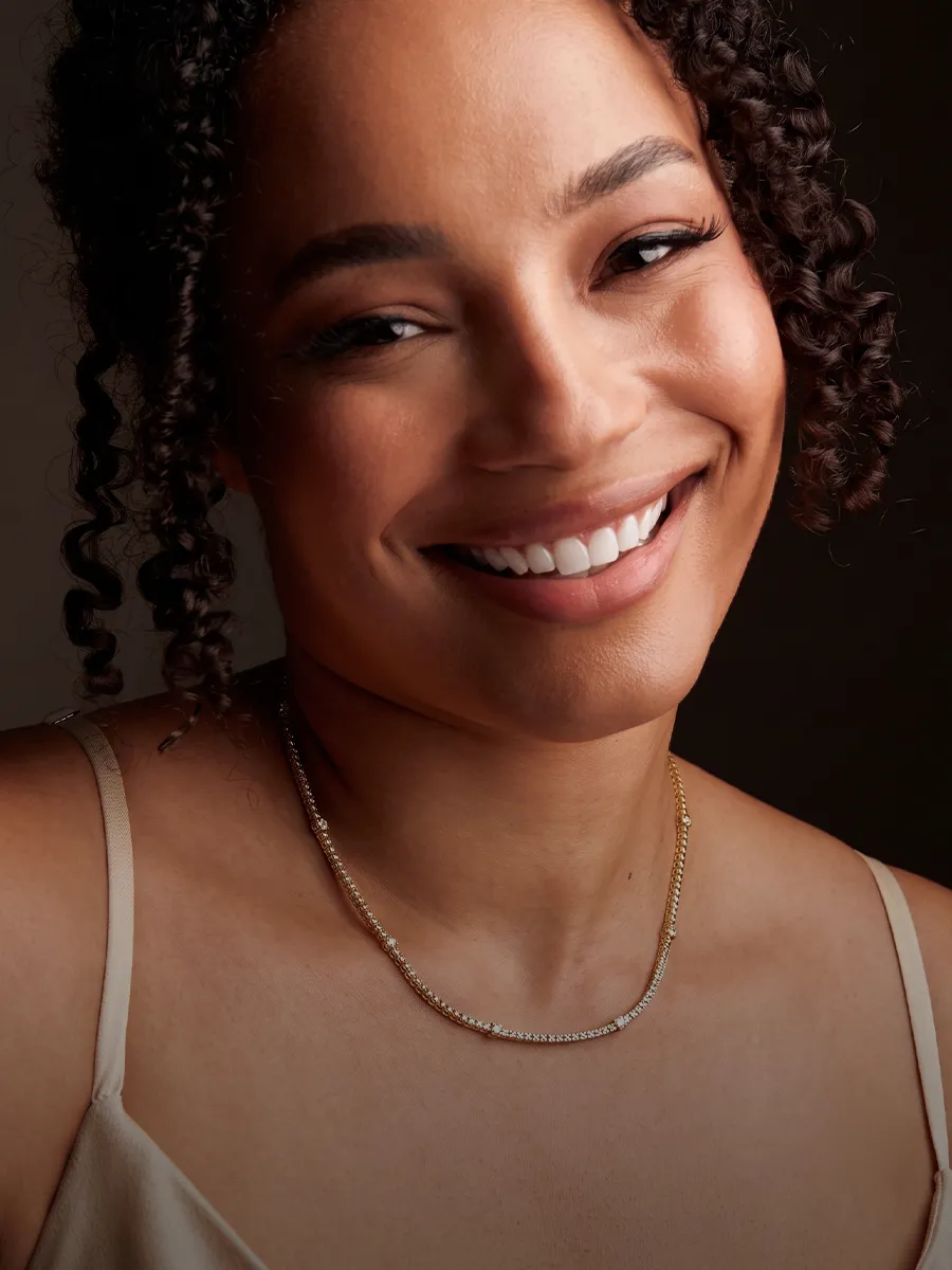 Smiling person wearing a delicate gold necklace with curls framing their face.