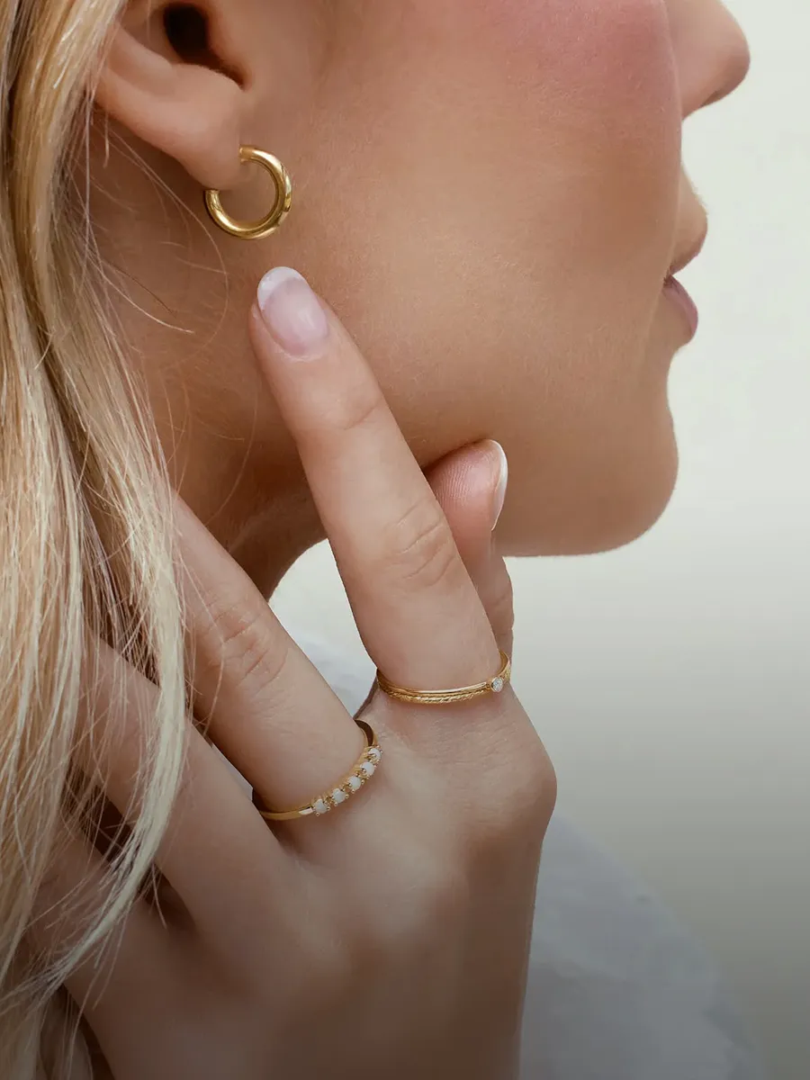 A person wearing gold hoop earrings and two gold rings with small stones.