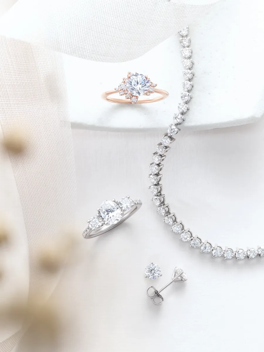 Elegant diamond jewelry set with rings, bracelet, and earrings on a soft fabric background.